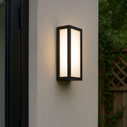 Outdoor wall light fixture on a textured wall with plants in the background