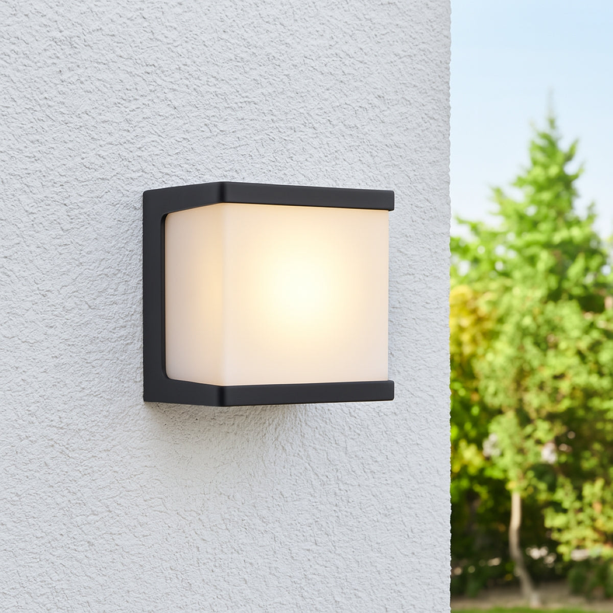 Outdoor wall light fixture on a textured wall with blurred greenery in the background