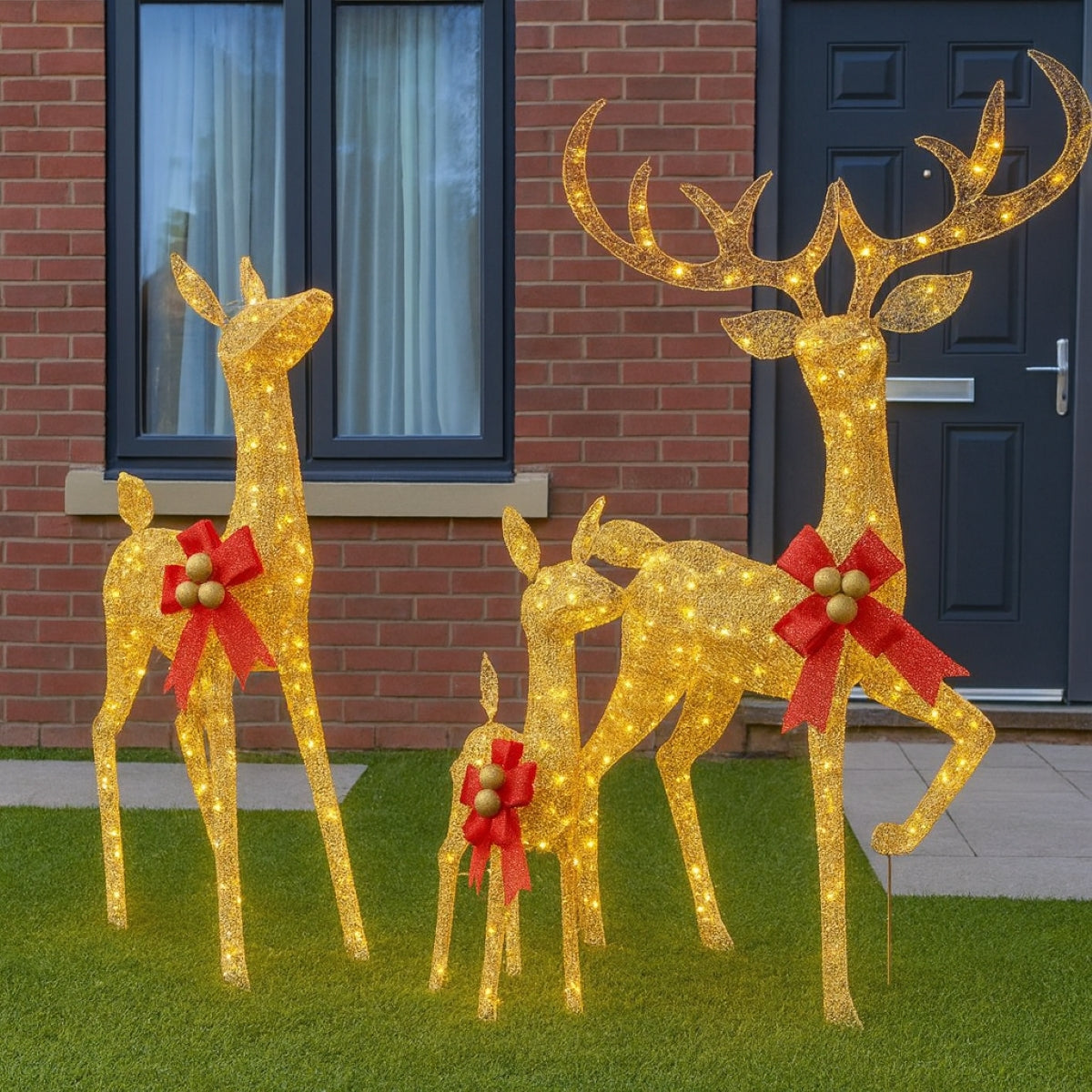 Decorative LED reindeer with red bows in front of a brick building.