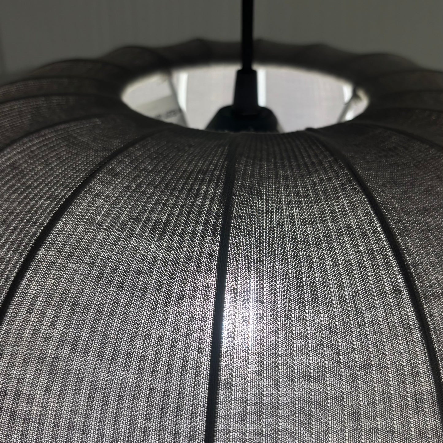 Close-up of a textured gray lampshade with a black cord against a neutral background