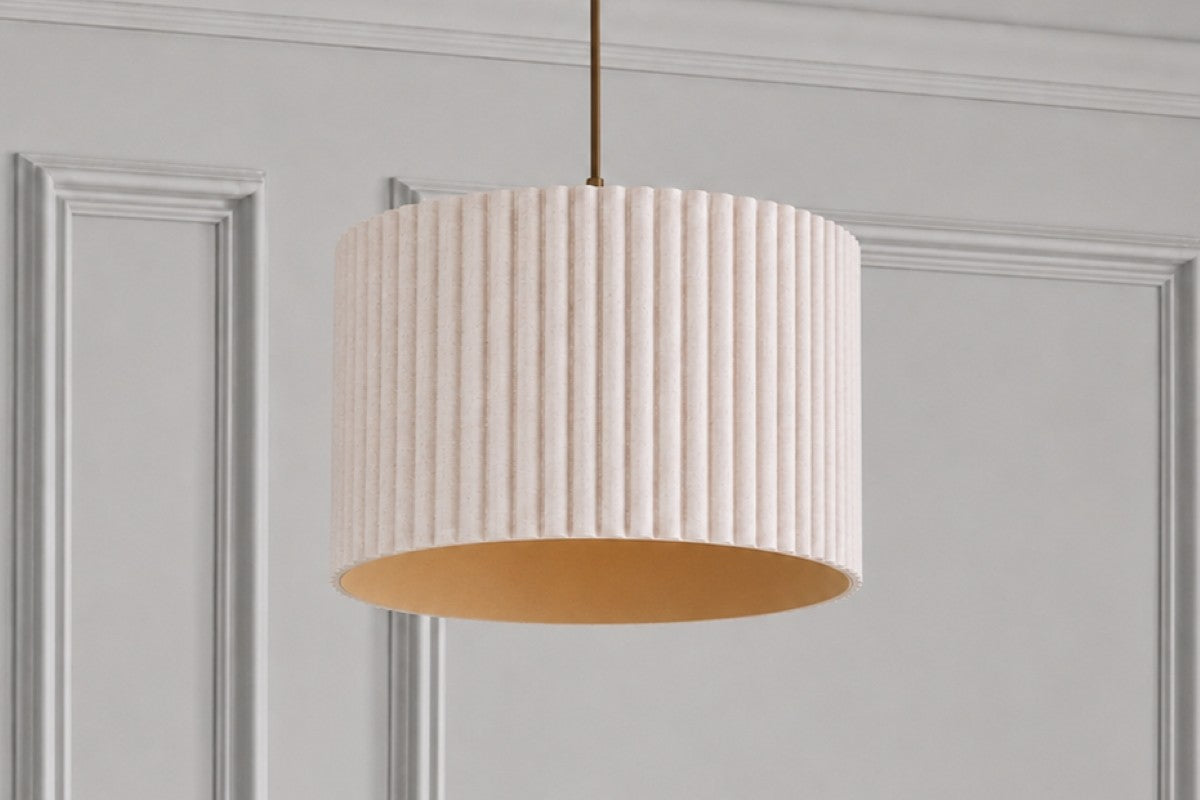 A modern white pleated pendant light hanging from a brass fixture against a textured beige wall and white ceiling.
