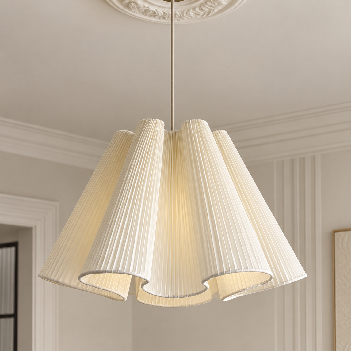 A modern multi-tiered pleated fabric pendant light in a warm cream color, hanging from a brass rod in a classic cream-colored room with decorative molding.