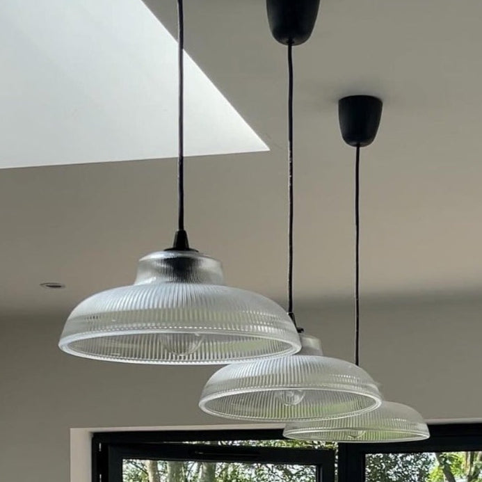 Clear glass ribbed lampshade suspended from the ceiling by wires, with light diffused through the glass.