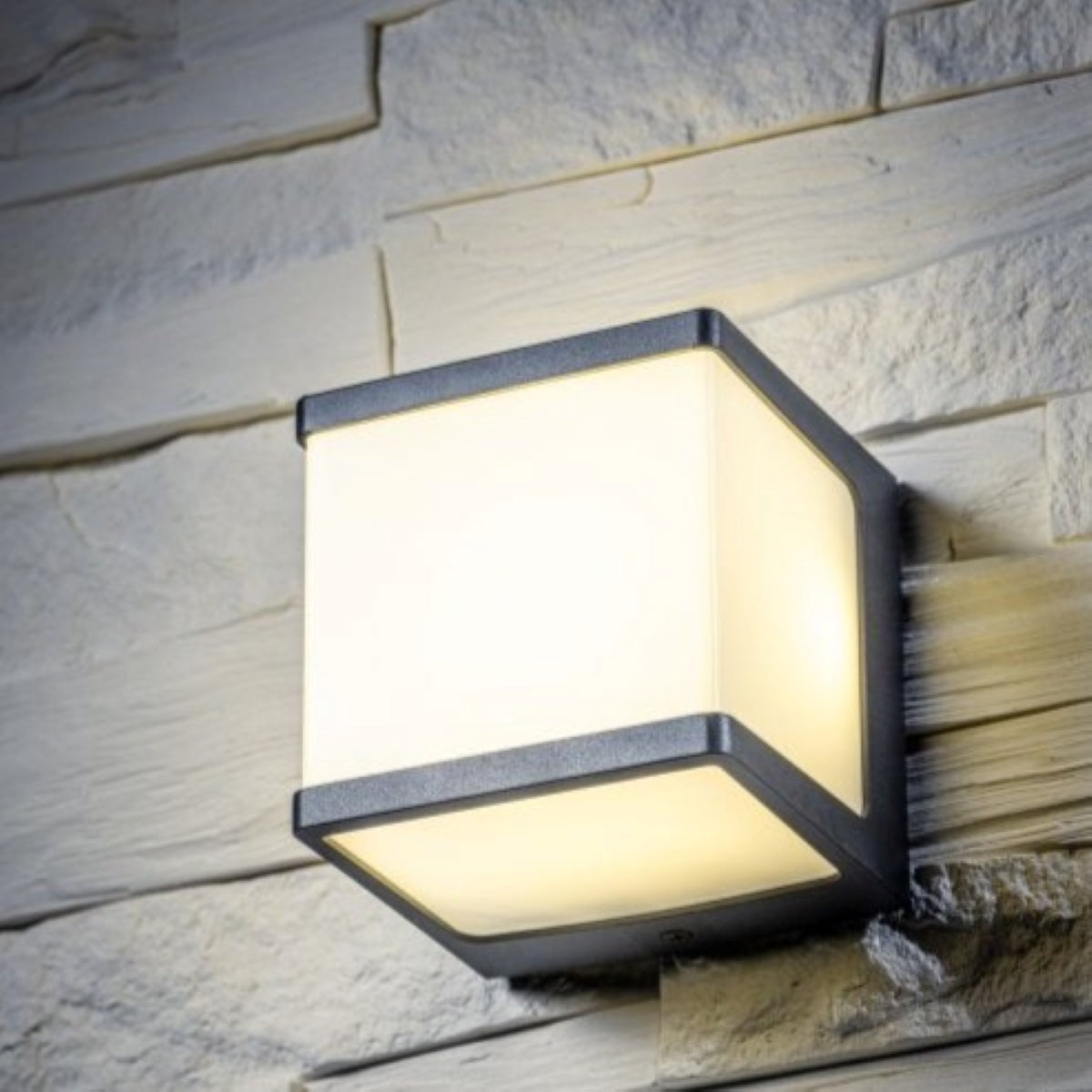 A black square LED outdoor cube wall light mounted on a brick wall, with an opal diffuser providing a natural white light.