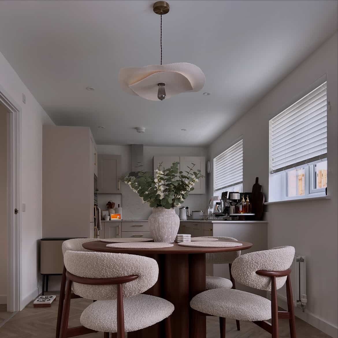 Modern kitchen with a round wooden table and chairs, featuring a vase with plants on the table.