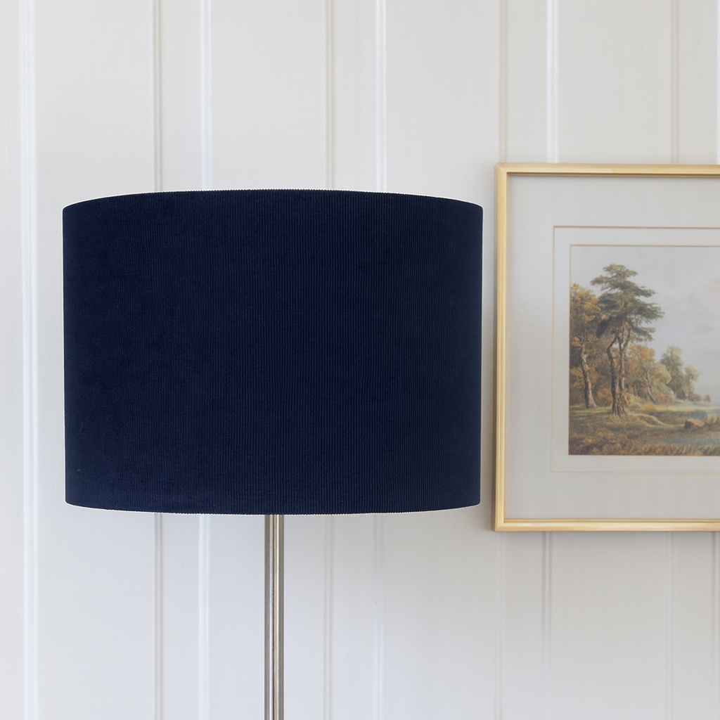 Navy blue lampshade on a white wall with a framed picture.