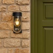 Wall-mounted outdoor light fixture on a stone wall next to a green door.