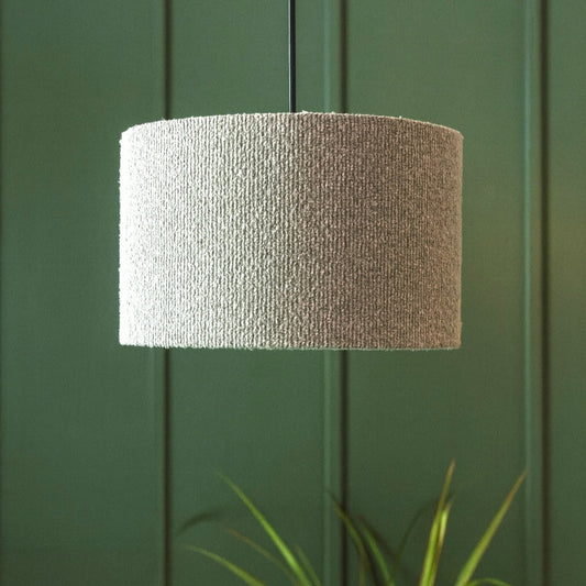 Textured lampshade against a green paneled wall with a plant in the foreground