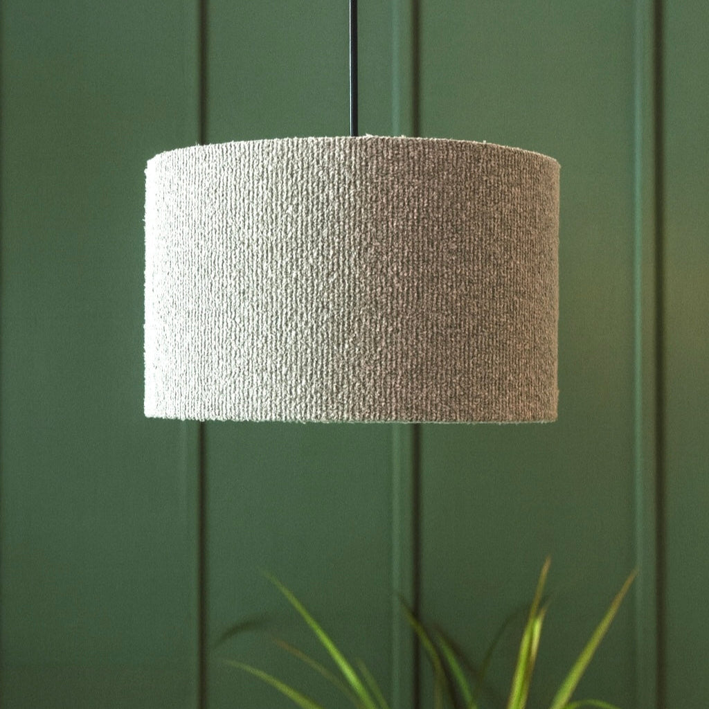 Textured lampshade against a green paneled wall with a plant in the foreground