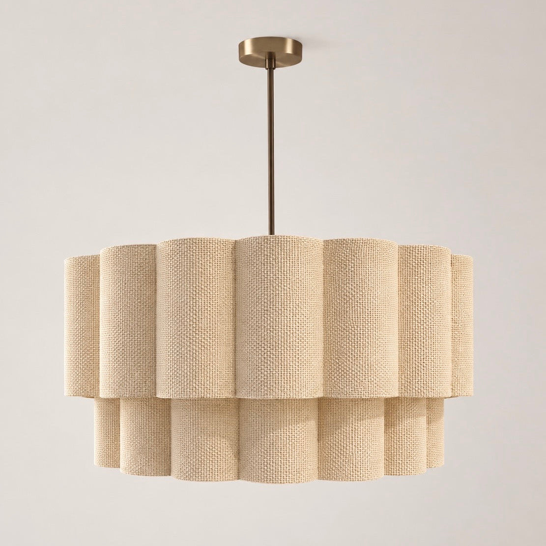 A modern multi-tiered drum chandelier with a textured beige woven fabric shade and a brushed brass ceiling canopy and rod, shown against a neutral off-white background.