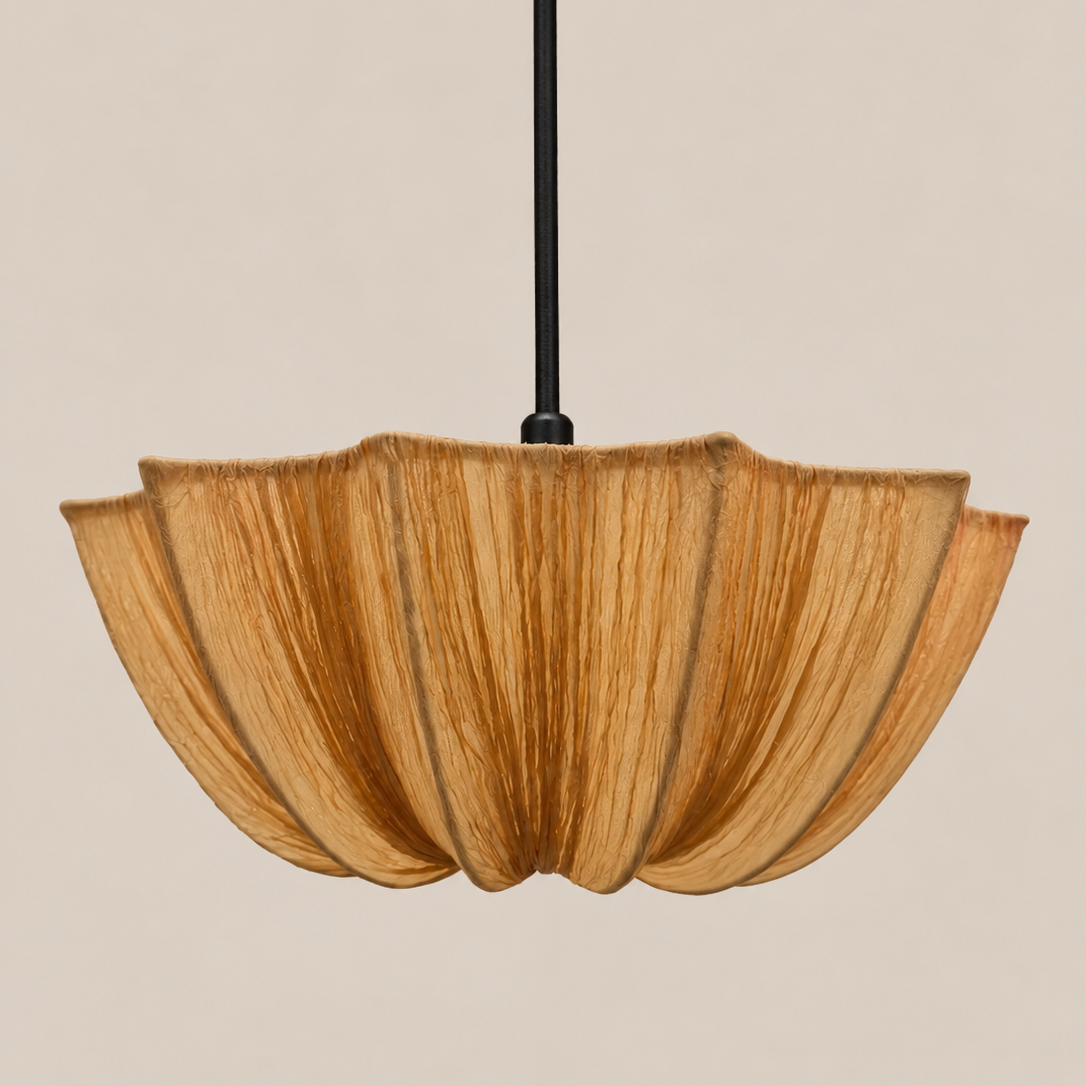 A modern pendant light with a pleated, petal-like shade made of natural wood, suspended by a thin black rod against a solid beige background.