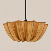 A modern pendant light with a pleated, petal-like shade made of natural wood, suspended by a thin black rod against a solid beige background.