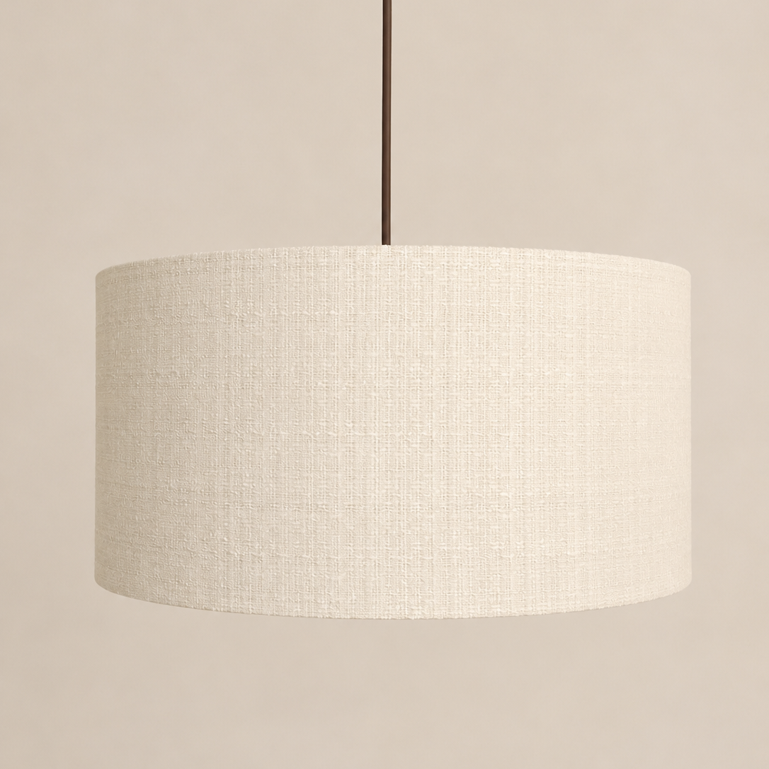 A drum-shaped pendant light shade made of textured cream linen fabric, suspended by a thin dark brown cord against a solid beige background.