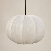 A white pleated paper pendant light hanging from a black cord against a warm beige background.