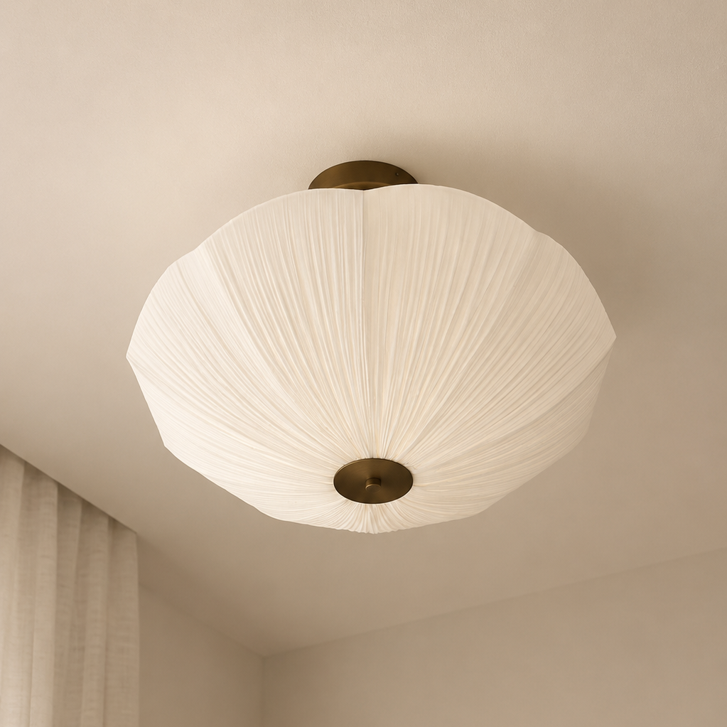 A modern ceiling light fixture with a pleated white paper lantern shade and brass metal accents, mounted on a beige ceiling in a minimalist room.
