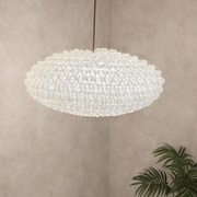 Large pendant light fixture hanging in a room with a plant on a neutral wall.
