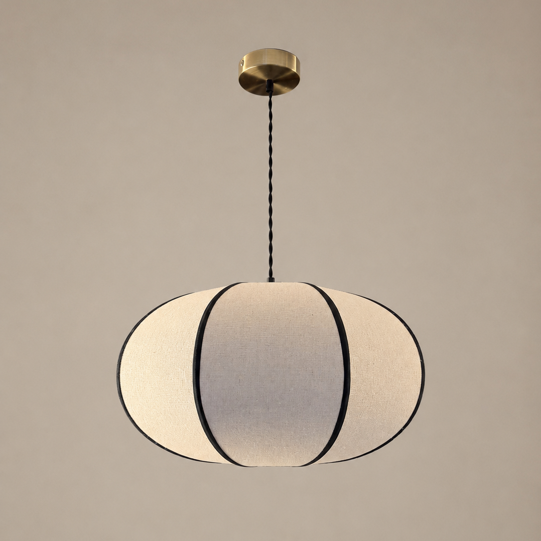 A modern pendant light with a ribbed, oval-shaped white fabric shade outlined in black, suspended from a brass ceiling canopy by a black cord against a neutral beige background.