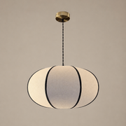 A modern pendant light with a ribbed, oval-shaped white fabric shade outlined in black, suspended from a brass ceiling canopy by a black cord against a neutral beige background.