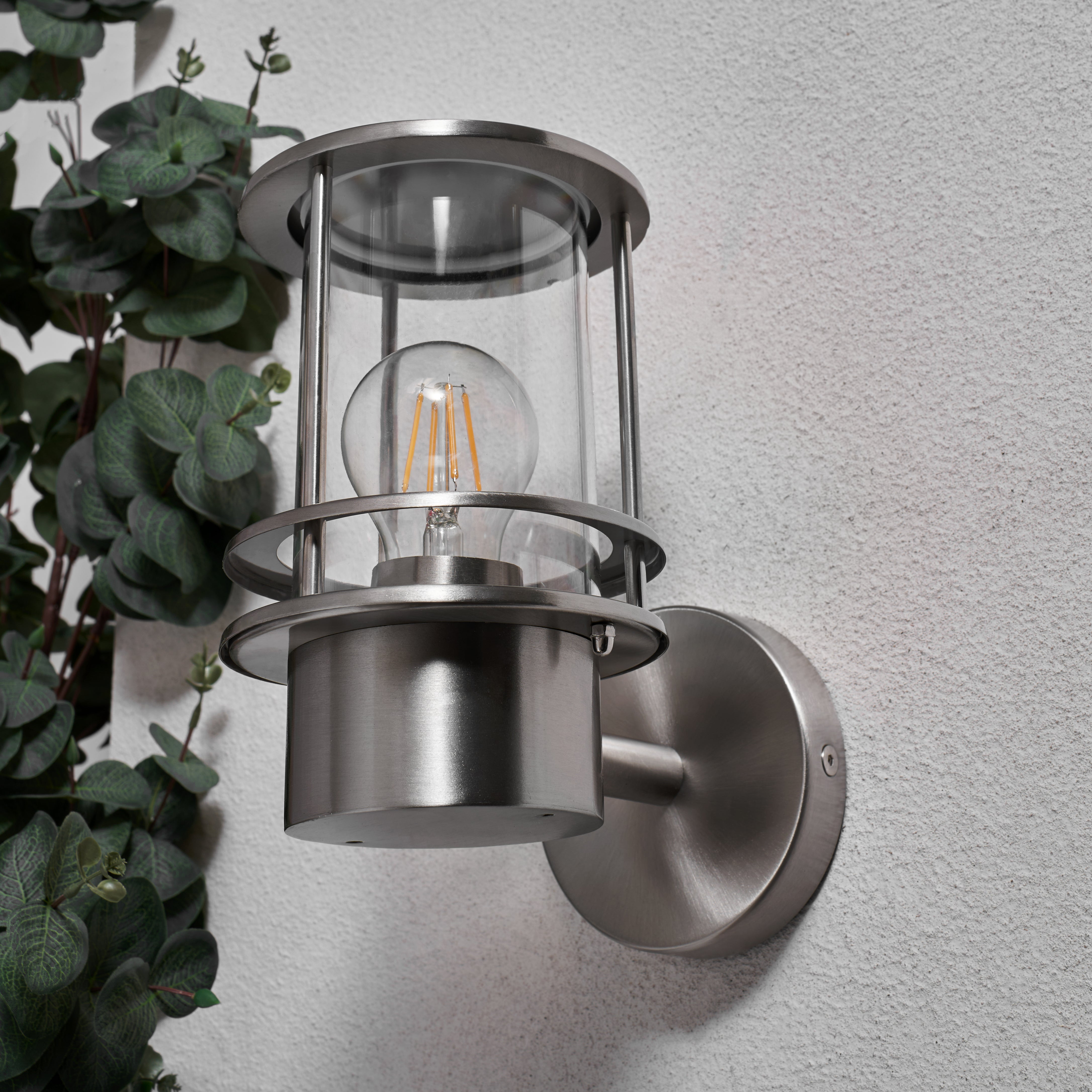 Outdoor wall light fixture on a gray wall with a plant to the left.