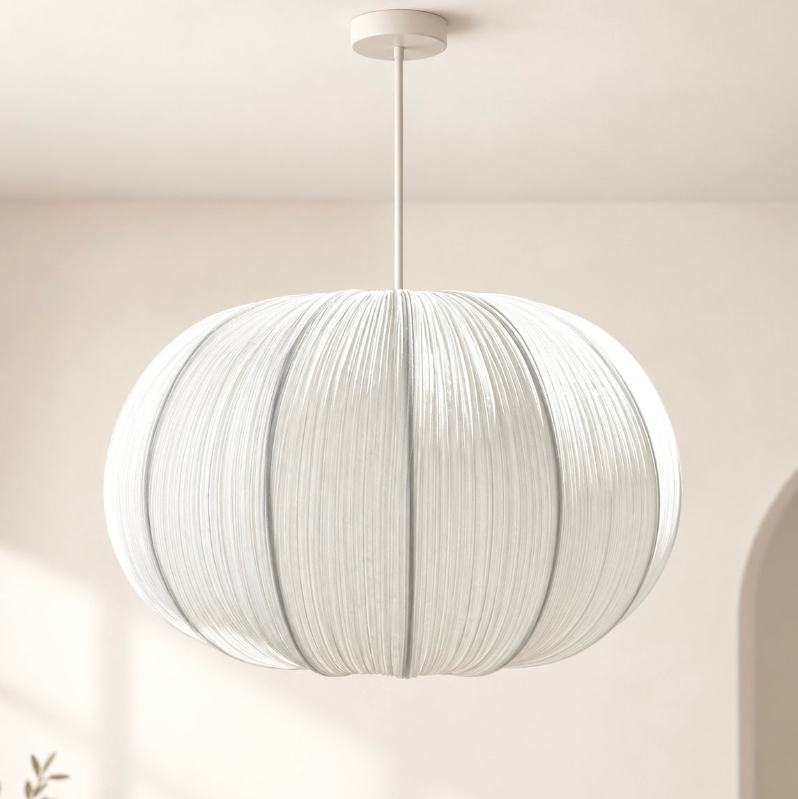 A white pleated paper globe pendant light hanging from a ceiling in a minimalist room with warm beige walls and soft window shadows.