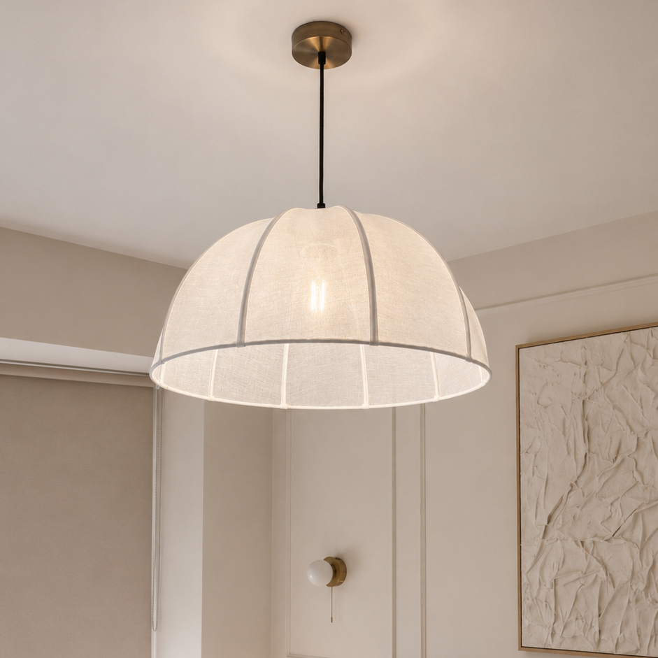 A modern dome-shaped pendant light with a textured off-white shade and a brass ceiling mount, hanging in a beautifully styled bedroom with neutral beige walls, a tufted headboard, and white bedding.