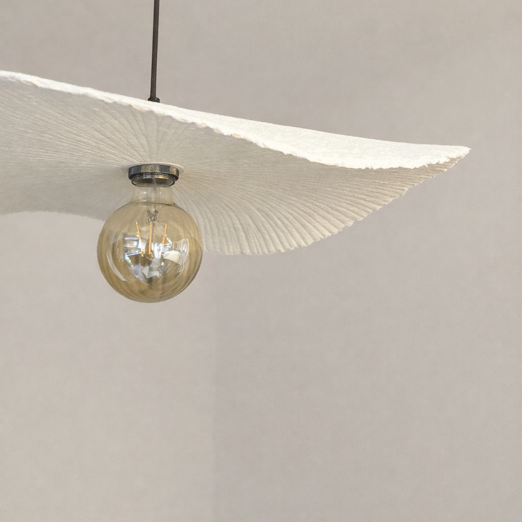 Modern pendant light with a white lampshade and clear glass bulb on a neutral background