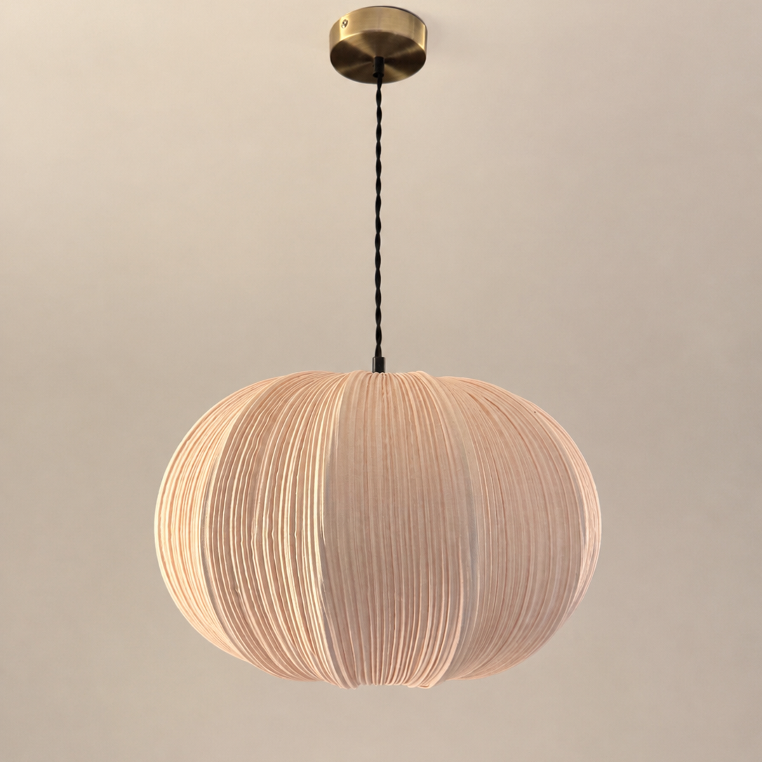 A modern spherical pendant light with a pleated beige fabric shade, suspended from a brass ceiling canopy by a black cord, set against a plain beige wall.