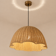A woven natural rattan dome pendant light hanging from a brass ceiling canopy, casting a warm golden glow and a circular light pattern on the ceiling.