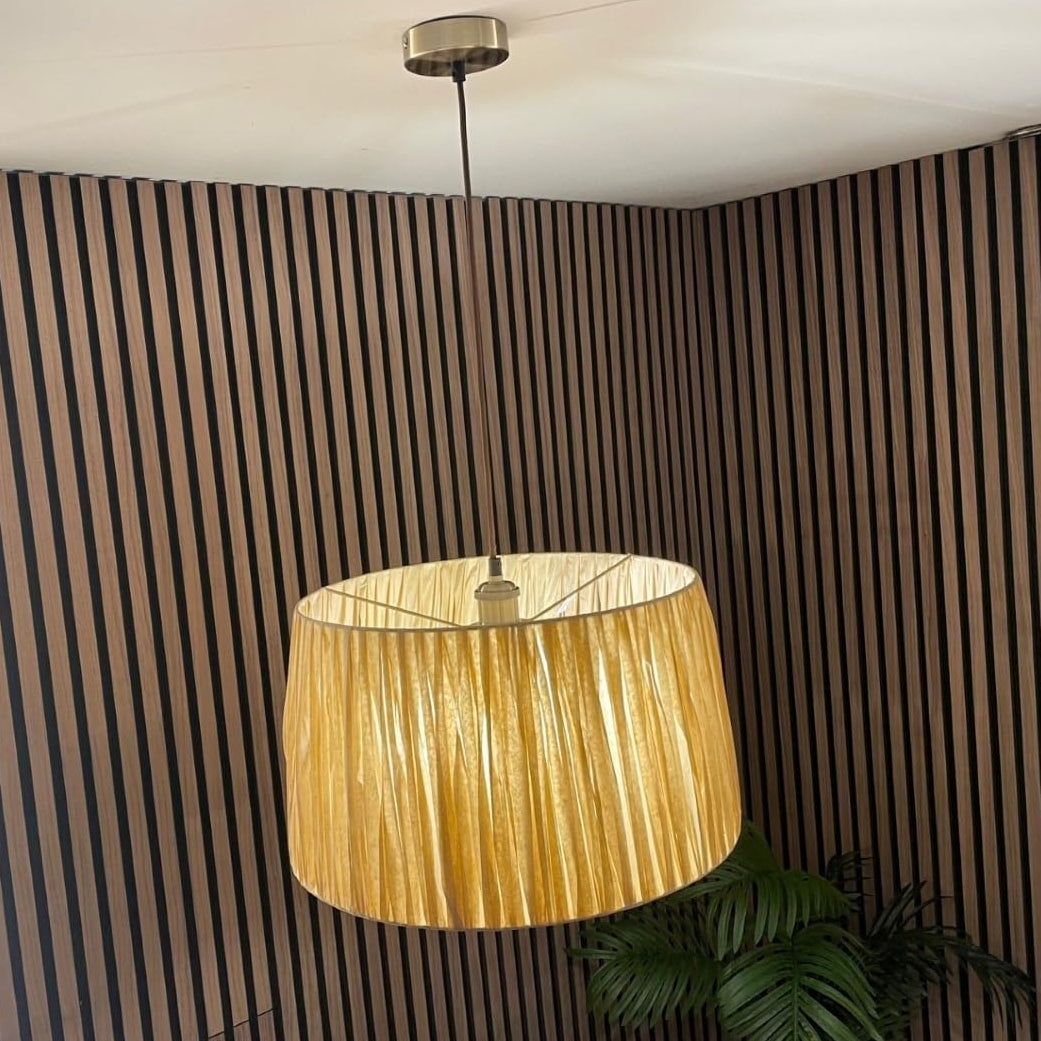 Gold pendant lamp hanging against a striped wall with a plant in the corner