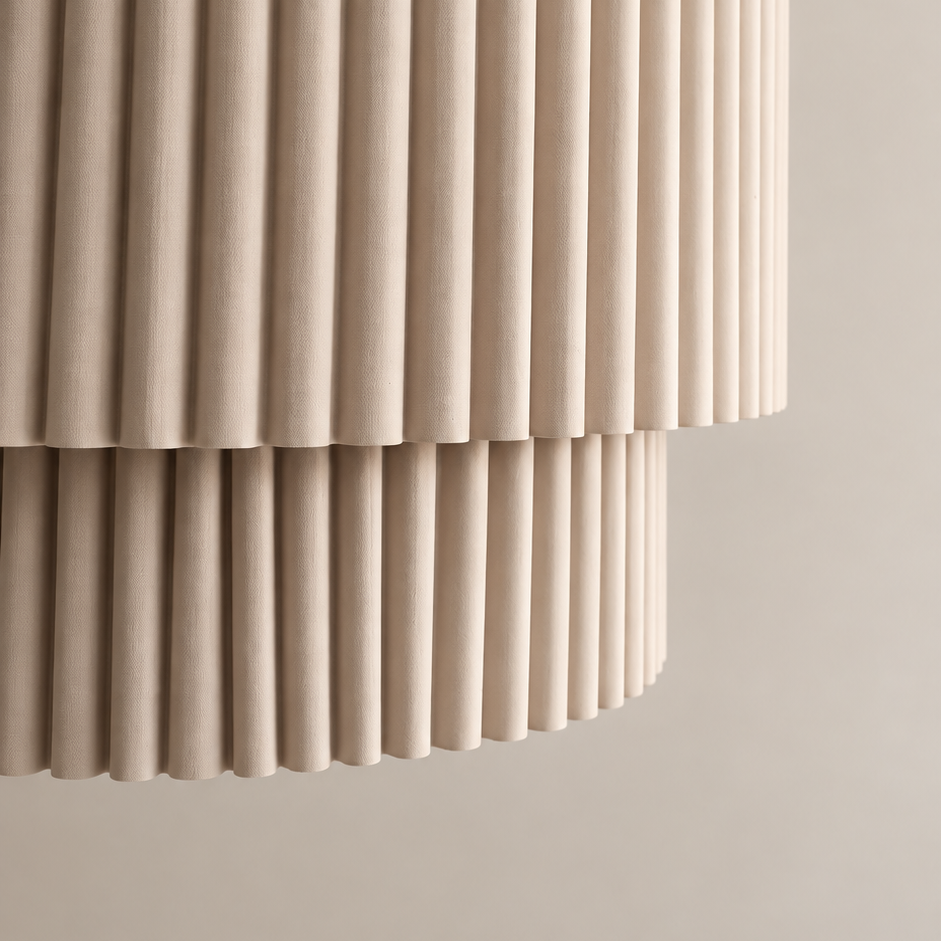 A close-up of a modern cylindrical pendant light with a fluted, pleated shade in a warm beige color, hanging against a matching beige wall.