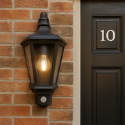 Black outdoor wall light fixture on a brick wall next to a door with the number 10.