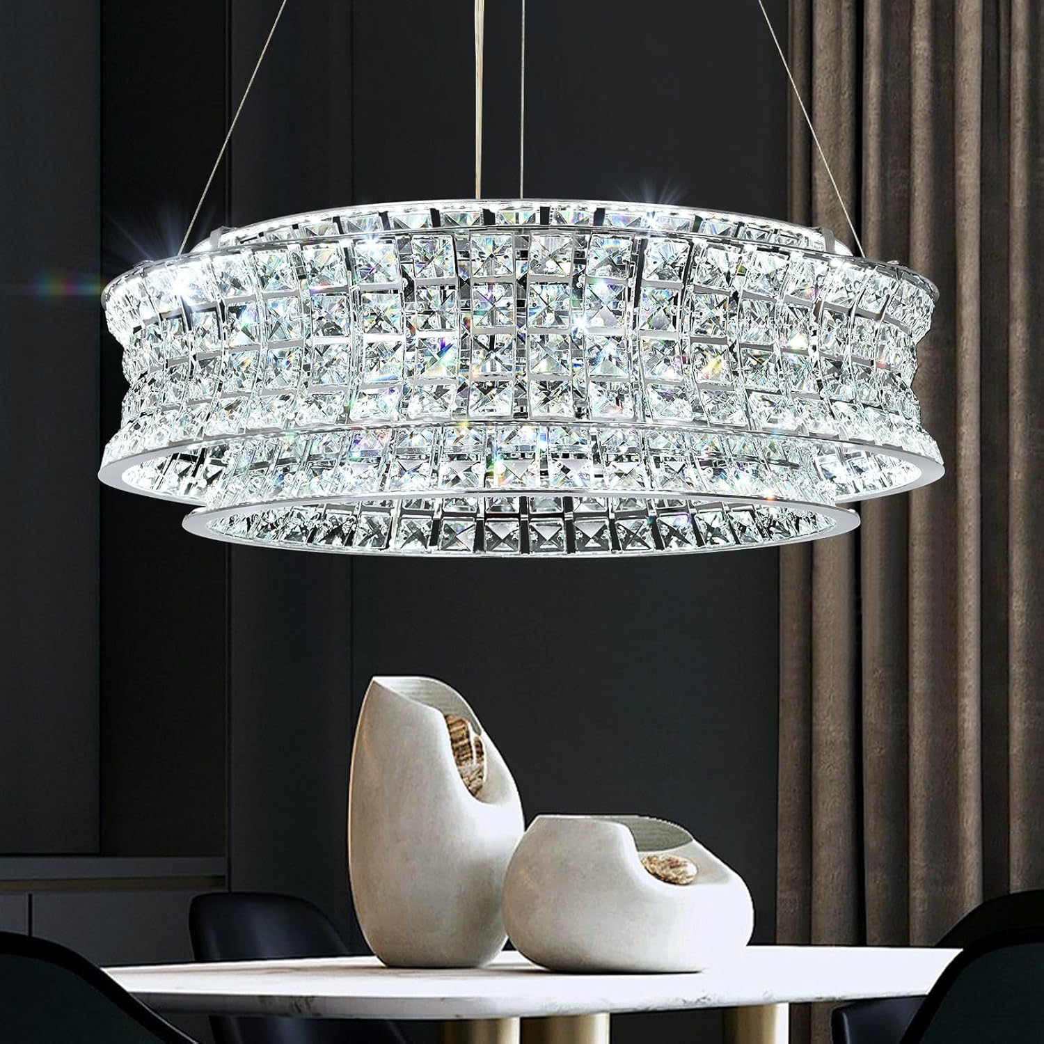 An elegant chrome and crystal adjustable ceiling light pendant with a circular design, hanging over a white table with decorative items.