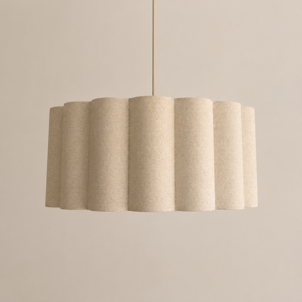 A modern pendant light with a fluted, pleated drum shade in a textured beige fabric, suspended from a brass fixture against a warm beige wall with a decorative white ceiling medallion.
