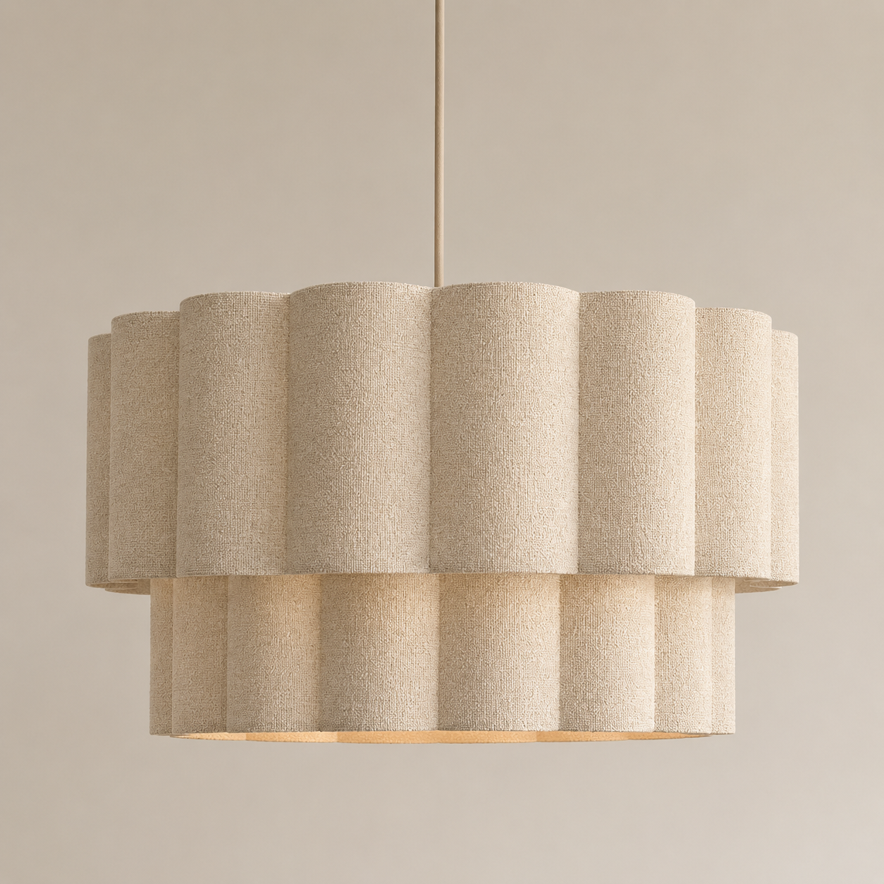 A modern drum pendant light with a textured beige fabric shade composed of overlapping cylindrical tiers, suspended by a thin cord against a solid beige background.