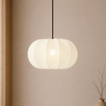 White pendant light hanging against a beige wall with a vase on the right.