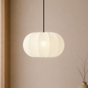 White pendant light hanging against a beige wall with a vase on the right.