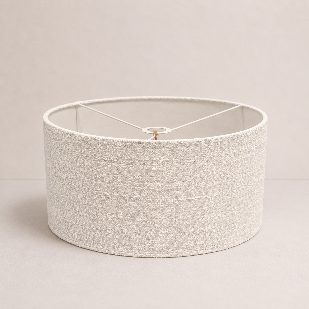 A close-up of a textured drum lampshade in a warm off-white or cream color, showing the woven fabric detail and the curved bottom edge.