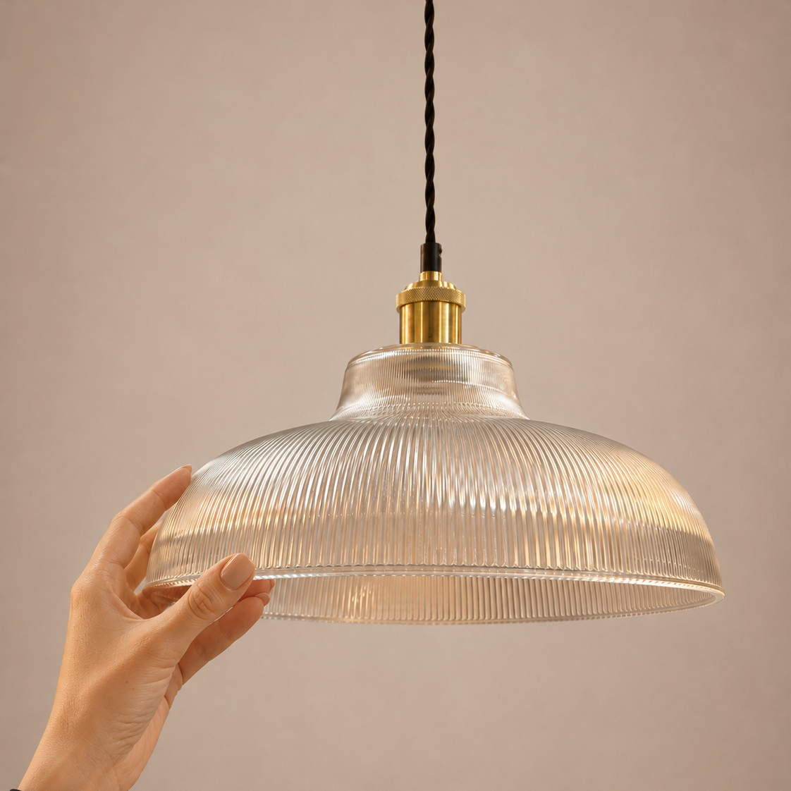 Hand holding a ribbed glass pendant light against a beige background