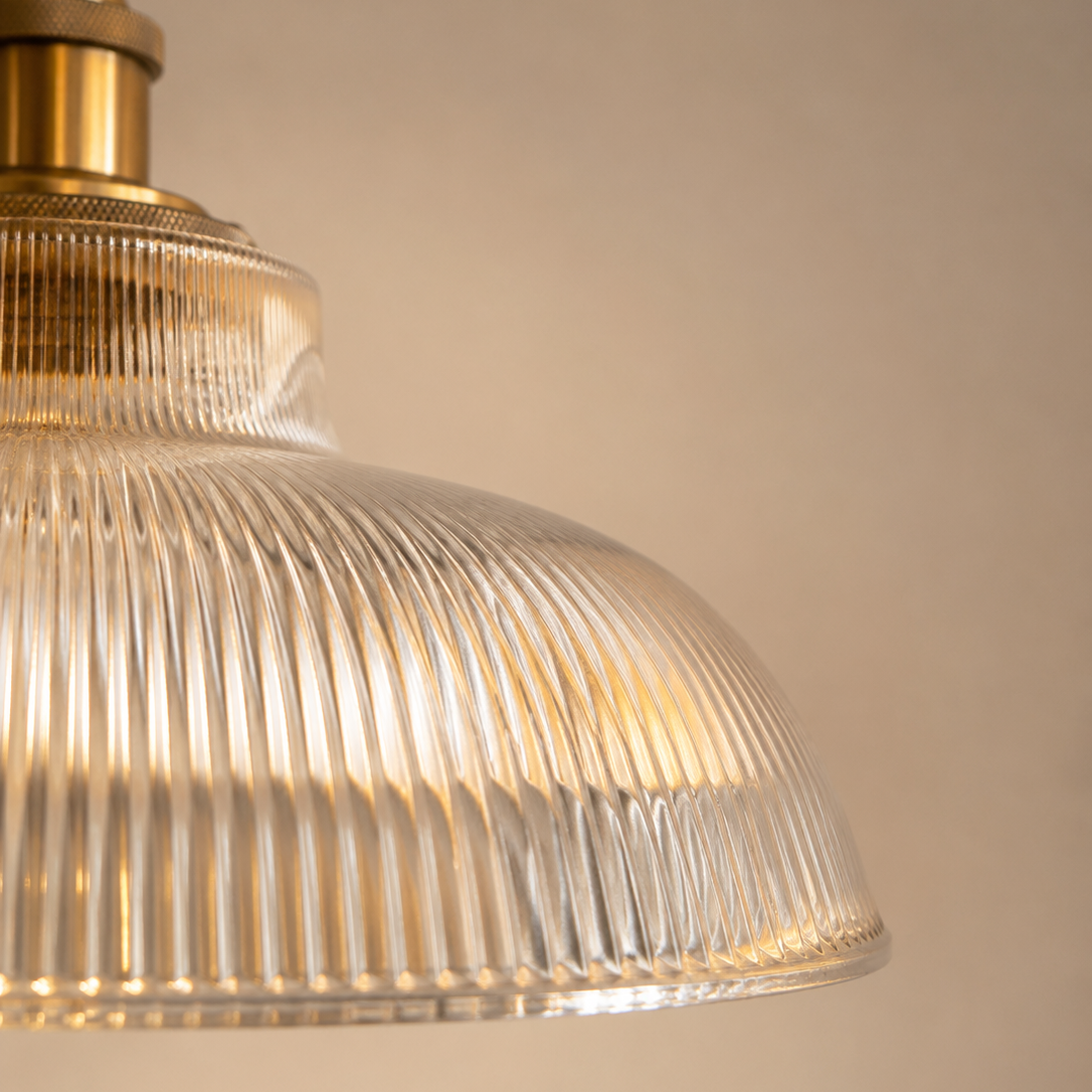 Close-up of a pendant light with ribbed glass shade and gold fixture on a beige background