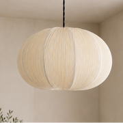 A modern spherical pendant light with pleated cream fabric and a brass ceiling canopy, hanging in a minimalist beige-toned room.