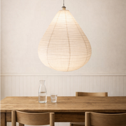 Wooden dining table with chairs and a pendant light in a room with a neutral wall.