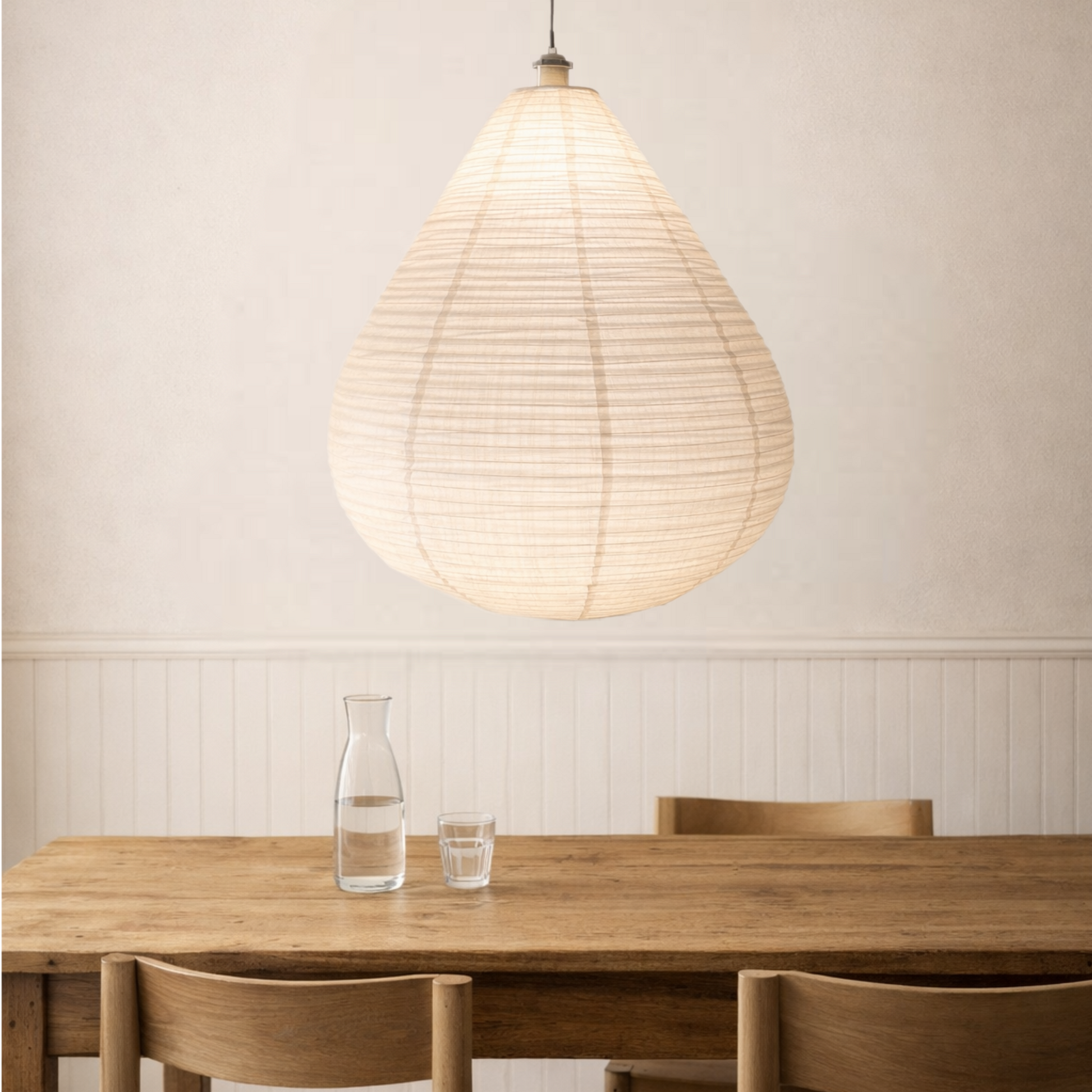 Wooden dining table with chairs and a pendant light in a room with a neutral wall.