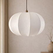 White pendant lamp hanging against a neutral wall with a vase on a shelf.