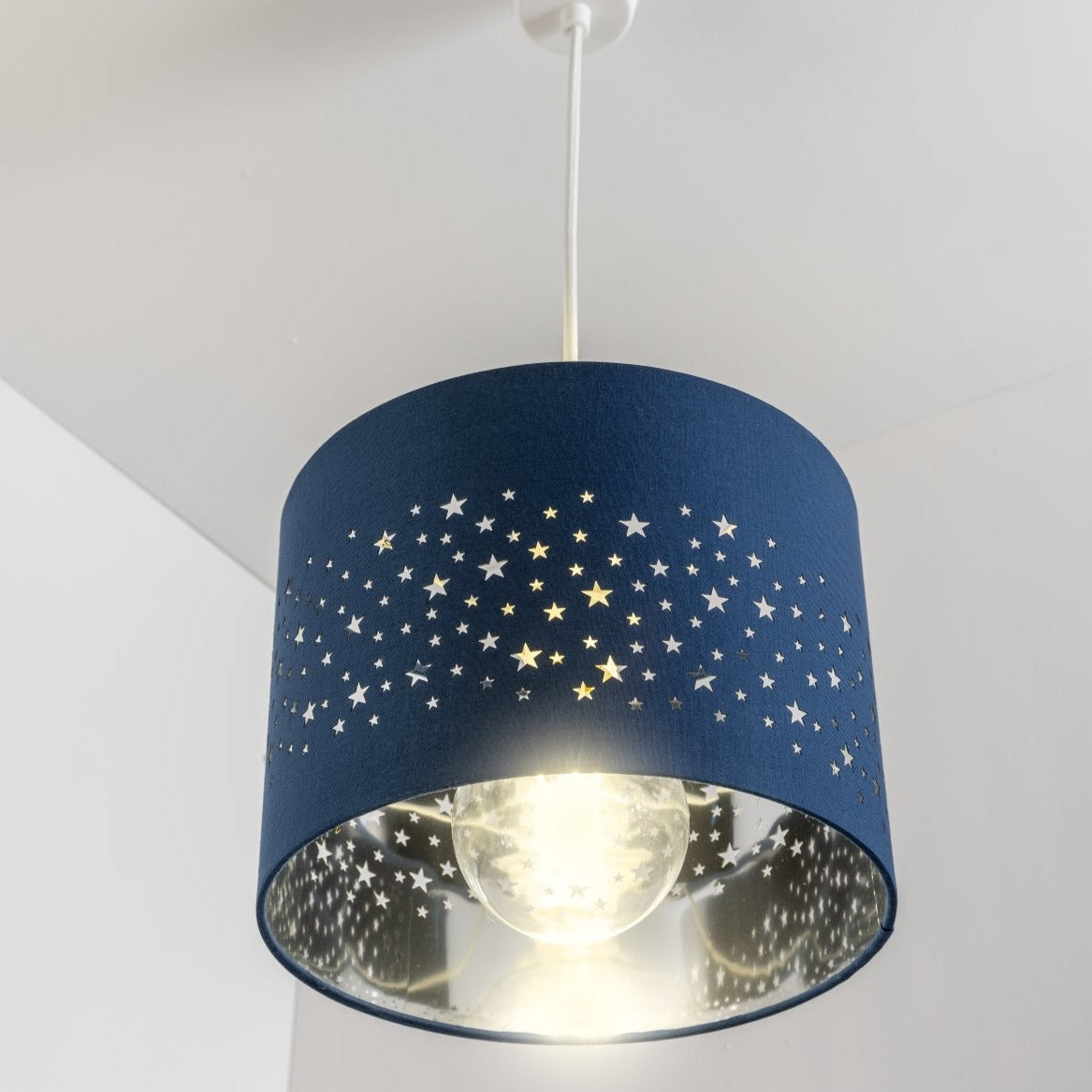 The Stardust luxury navy fabric star pendant shade would make a charming touch to your room. Constructed from a high quality soft navy cotton material with intricate laser cut stars in various sizes making a stunning effect in the room when lit. This easy fit non electrical pendant lampshade and can simply be fitted over any standard light fitting or table lamp.