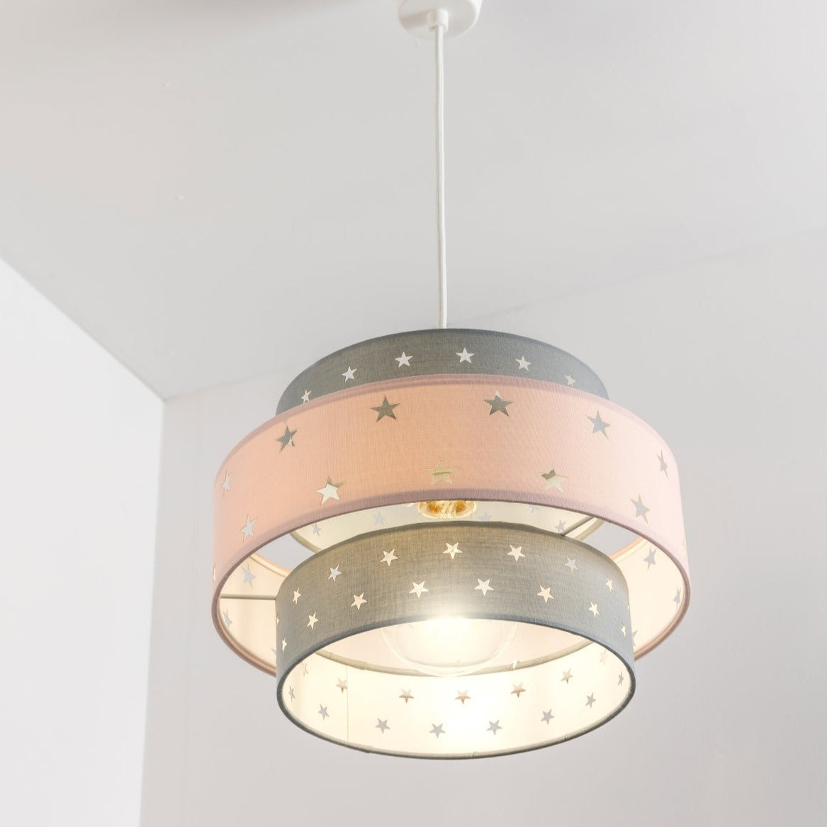 Our grey and pink two tiered star shade features a mixture of large and small sweet stars cut out across a grey and pink background. When your lamp is turned on it will shine out through these cut-outs, mimicking a beautiful night sky. This lampshade is made with soft-touch fabric for a little bit of luxury.