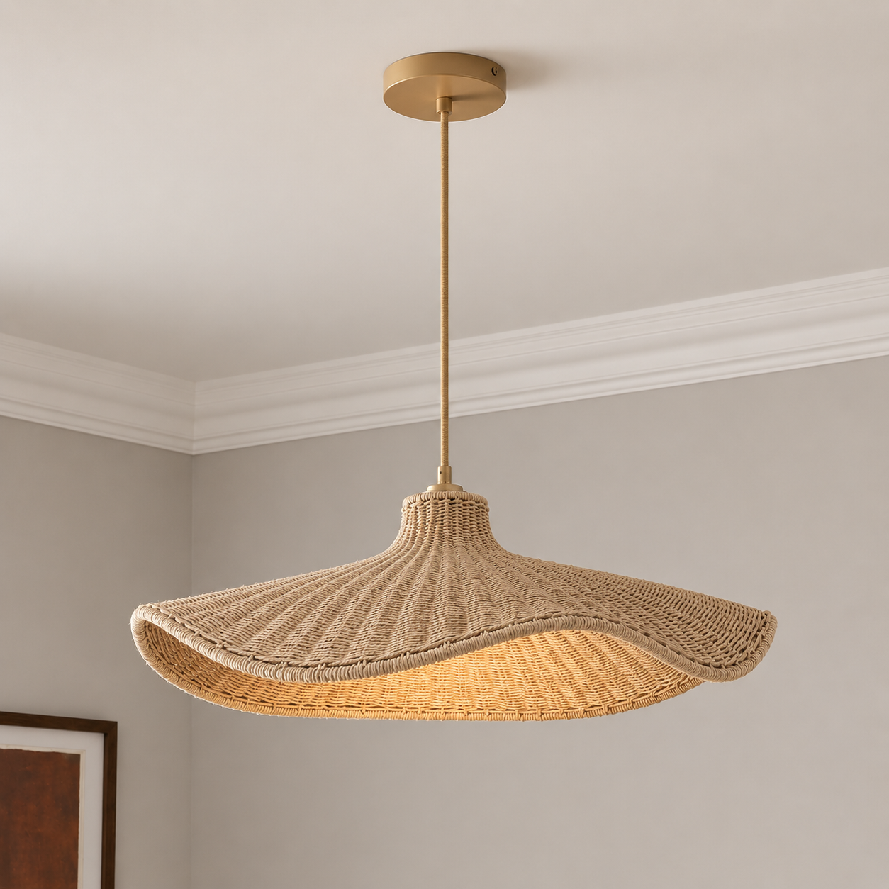 A pendant light with a wide, wavy woven natural-fiber shade and a warm brass-toned metal canopy and rod, shown hanging in a room with light gray walls and white crown molding.