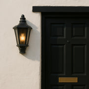Black door with a wall-mounted light fixture on a beige wall