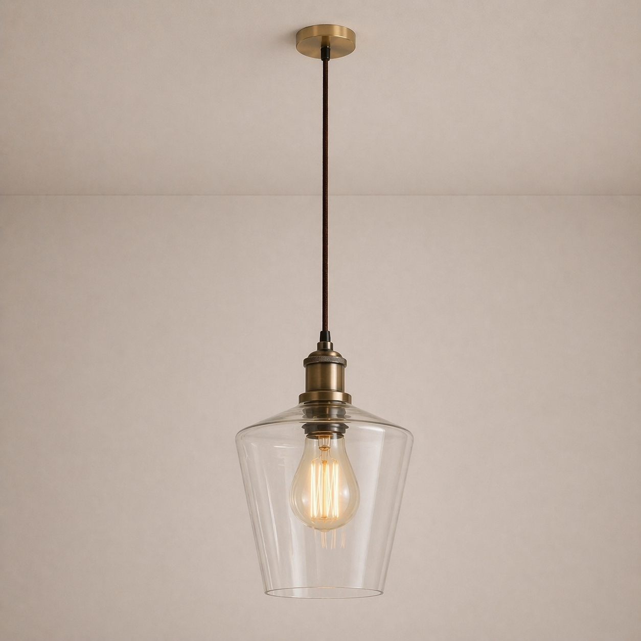 Pendant light with clear glass shade and brass fixture on a beige background