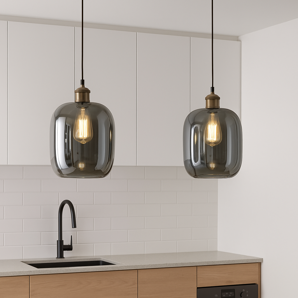 Two hanging pendant lights in a kitchen setting with white cabinets and a sink.