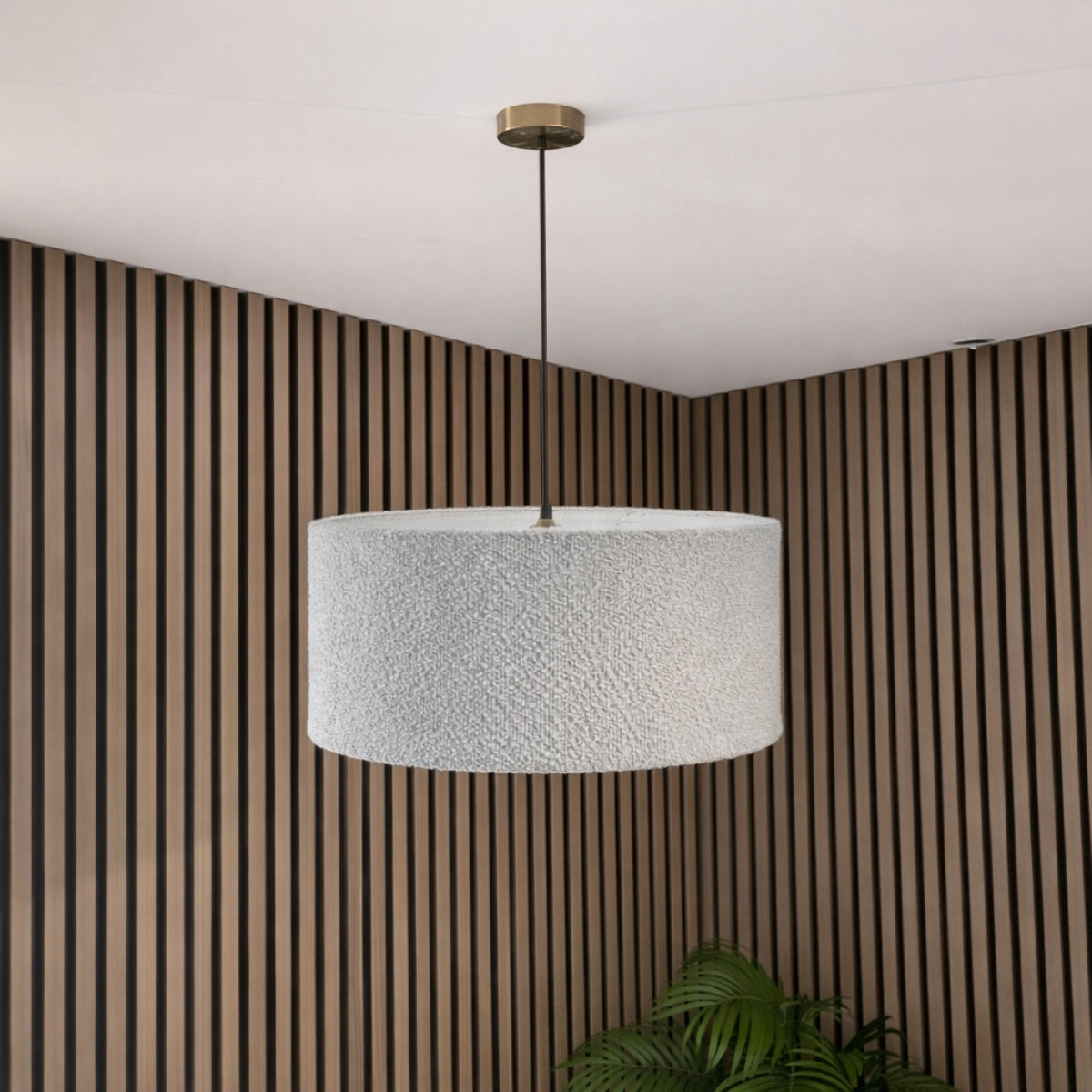 Textured pendant light hanging against a striped wall with a plant in the corner.